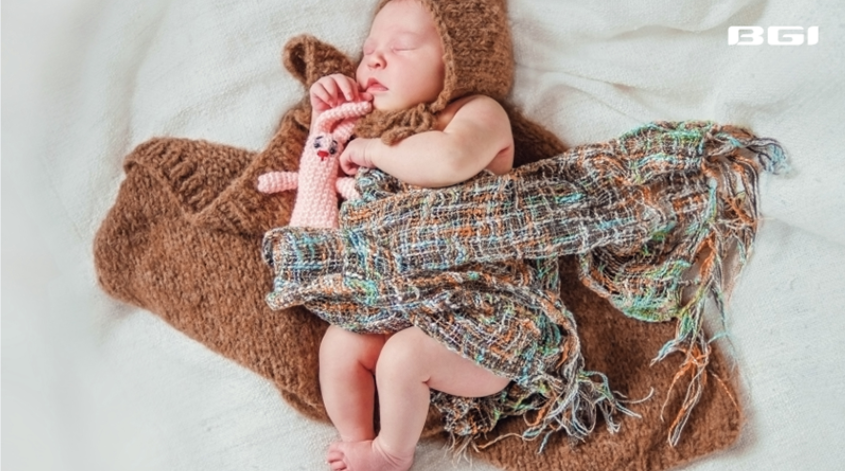 Sleeping newborn wearing a knitted bear bonnet, wrapped in a blanket